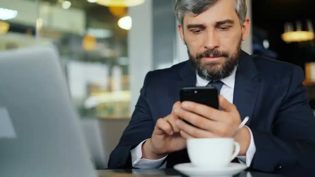 カフェのテーブルで、スマートフォンとクレジットカードを使いオンライン決済をしている男性