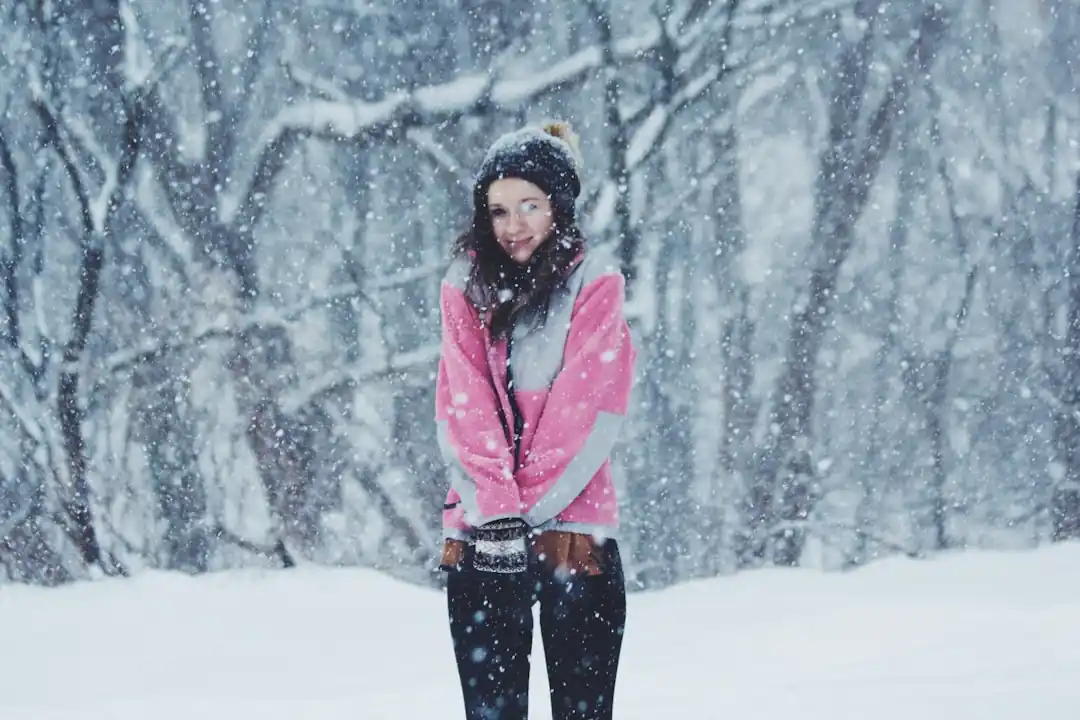 ピンク色の暖かいジャケットを着て、雪景色の中で空を見上げる女性