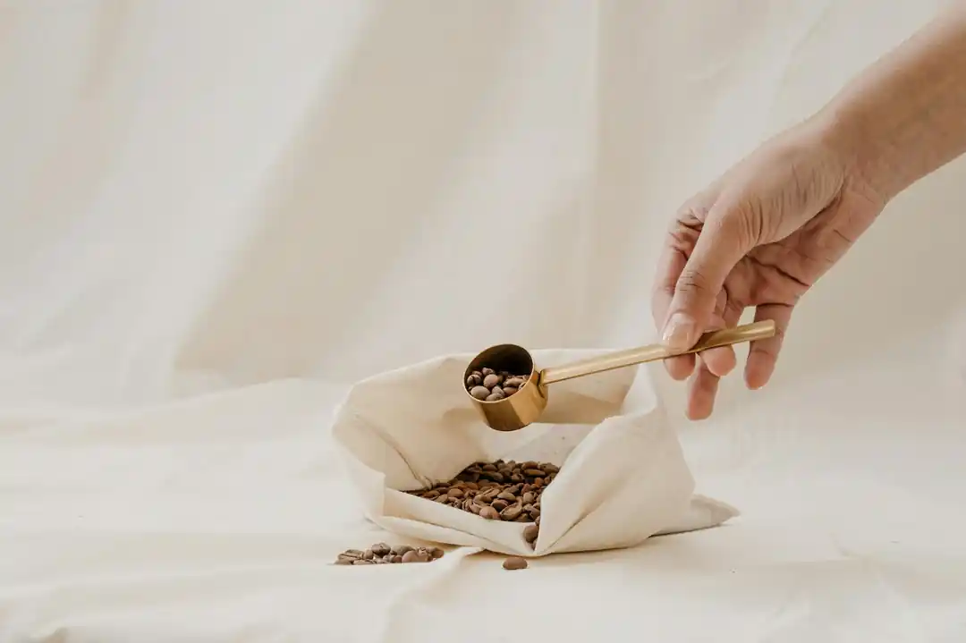 一隻手拿著木勺,從布袋中舀取天然材質的貓砂顆粒。