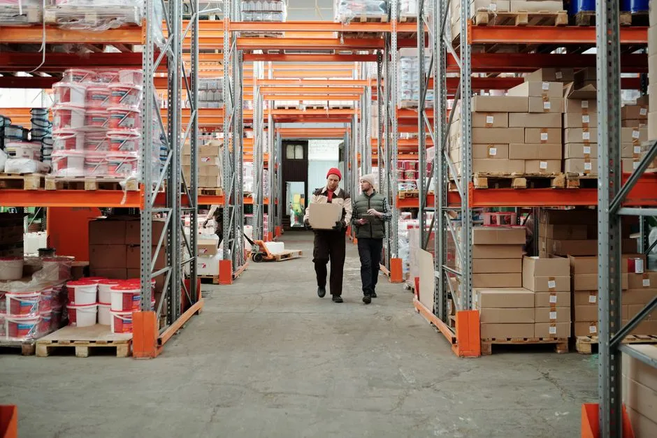 Two warehouse employees organizing boxes on tall storage shelves.