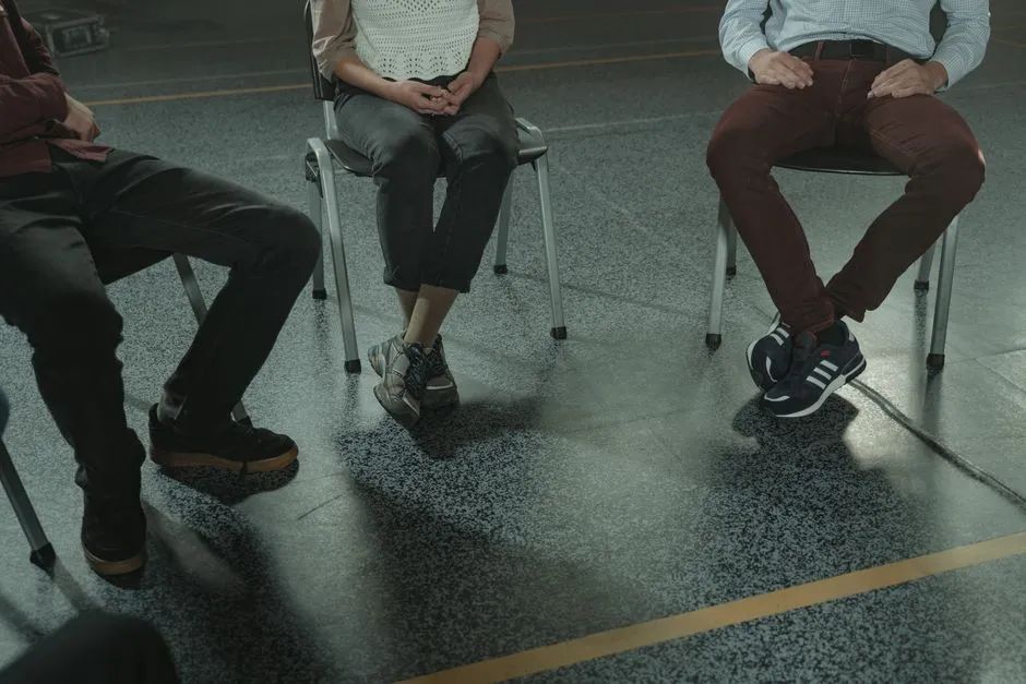 A group of three adults sitting in chairs during a discussion or support session indoors.