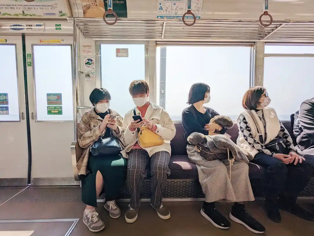 夜行バスのような乗り物の中で、窓の外を眺めたり、スマートフォンを見たりして過ごす若者たち