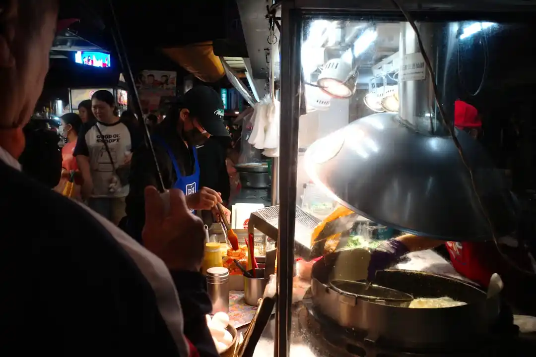 一位攤販正在熱鬧的台灣夜市裡專注地準備著手中的食物。