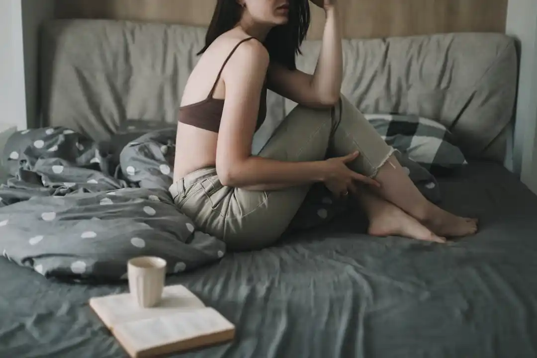 ベッドの上で、温かい飲み物の入ったカップを片手に本を読んでいる女性