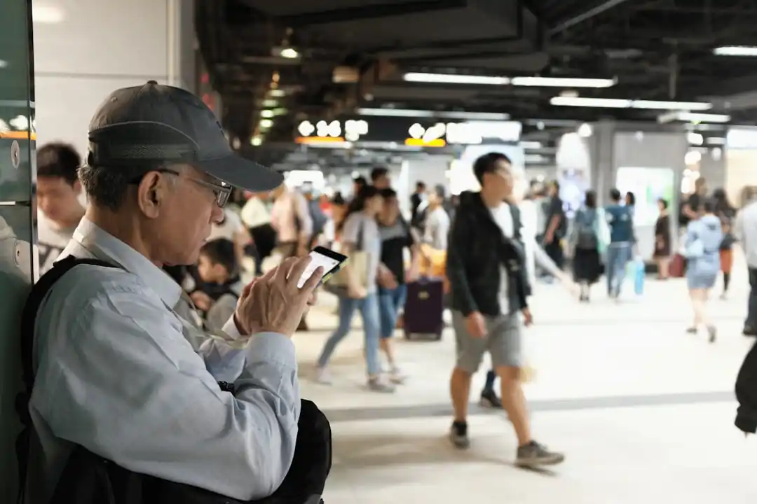 ホームで電車を待ちながらスマートフォンを見る男性