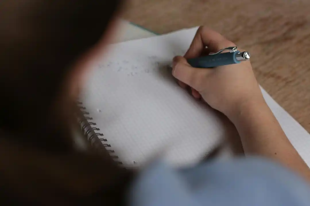 ペンを手に持ち、ノートに数式を書き込んでいる様子