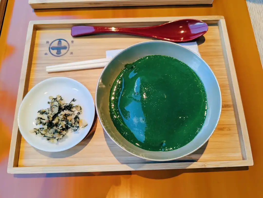 一碗翠綠色的湯品,旁邊放著一碟小菜和湯匙。