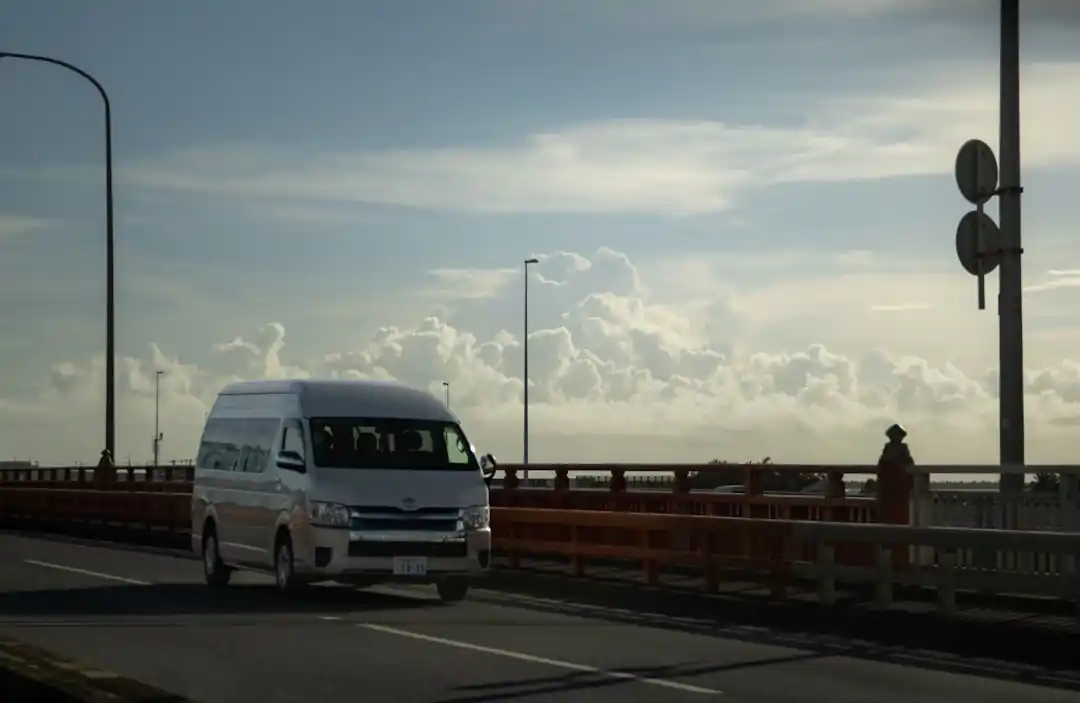 沖縄の道路を走る白いバス。背景には交通信号機と建物が見える。